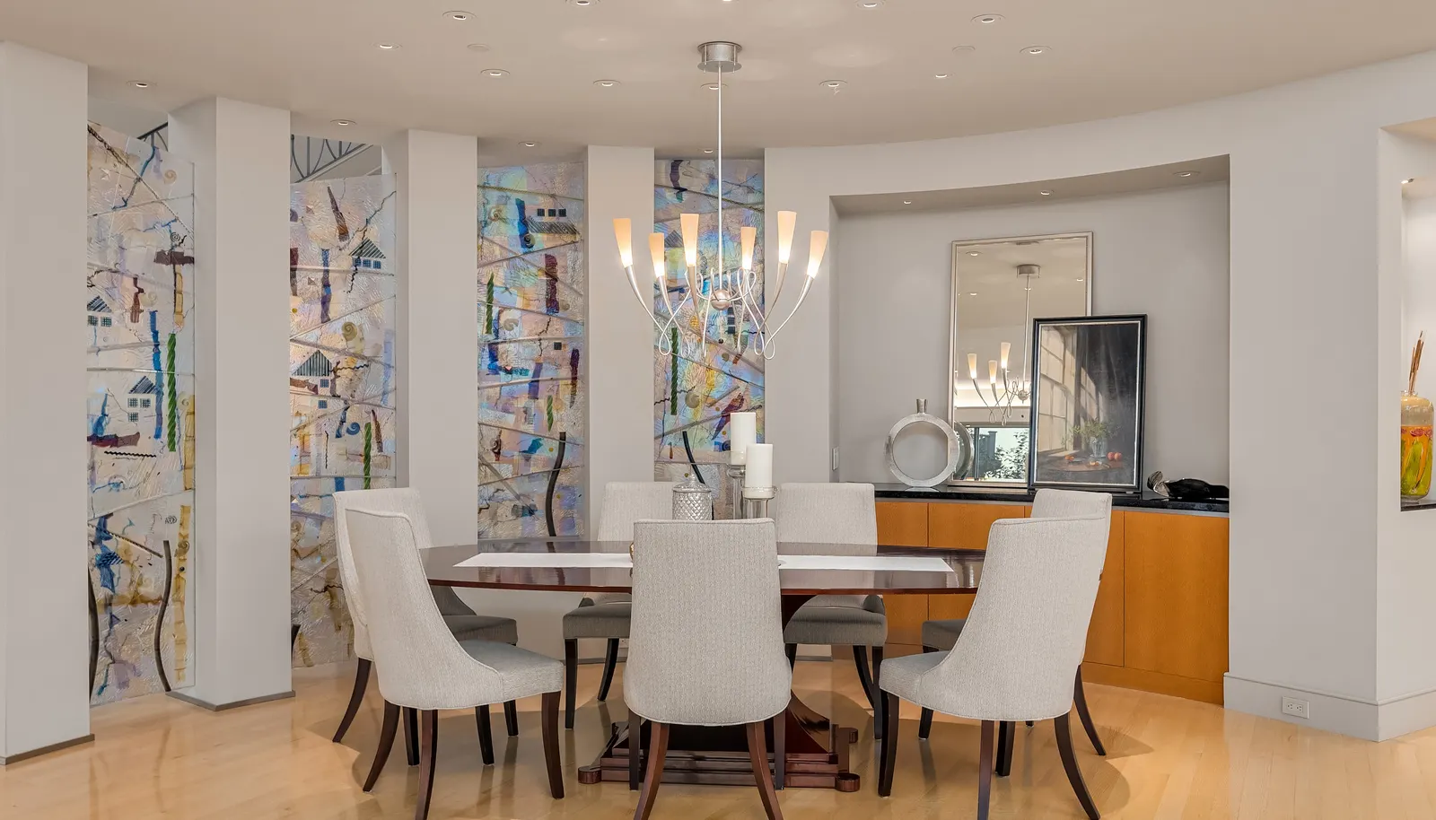 This home, and the main floor specifically, was designed with entertaining in mind. There are 12 spotlights in the ceiling that point down to the 12 seats at this oval table...(in fact, there is a whole home Lightolier Control system where multiple scenes can be programmed per room, floor or whole house). The glass art walls were commissioned & designed by Seattle glass artist, Gary Newcomb, and provide a playful and fun backdrop that is edge lit from above to maximize the surface texture. Notice the curved built-in buffet and art niche in this space.